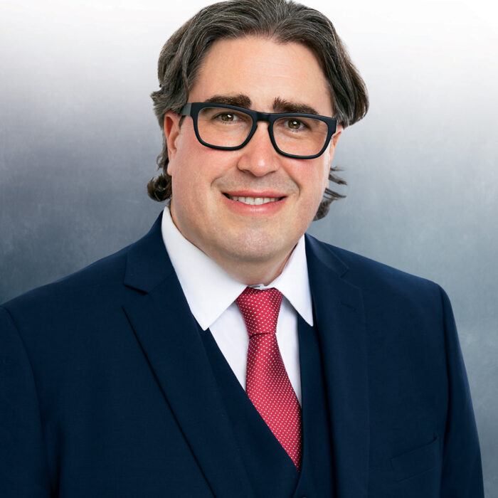 white male with glasses wearing a. navy blue suit and red tie