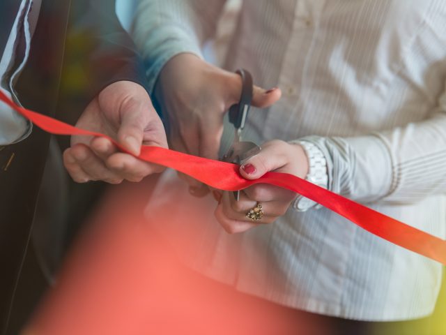 Woman is cutting a red ribbon with scissors.